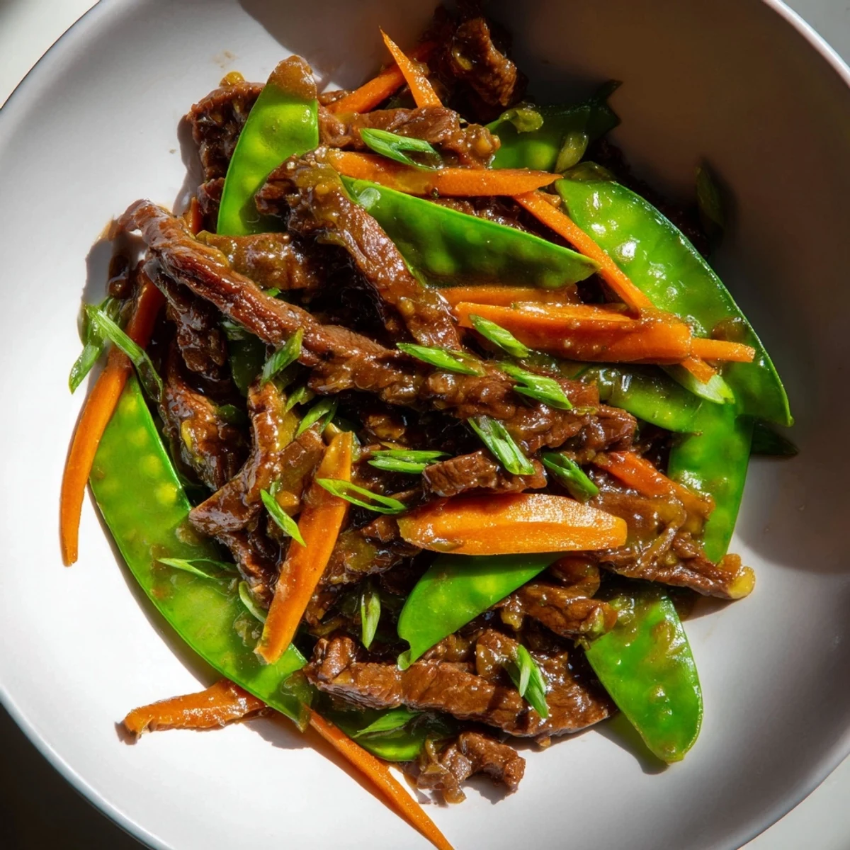 Delicious beef stir fry, showcasing tender beef, vibrant snow peas, and carrots in a glossy sauce.