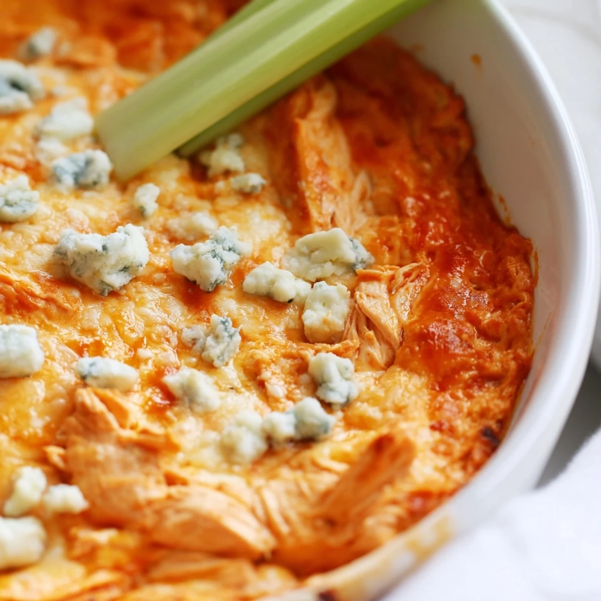 Spicy Buffalo Chicken Dip with celery sticks on a platter, featuring melted cheese and a tangy, fiery red buffalo sauce.