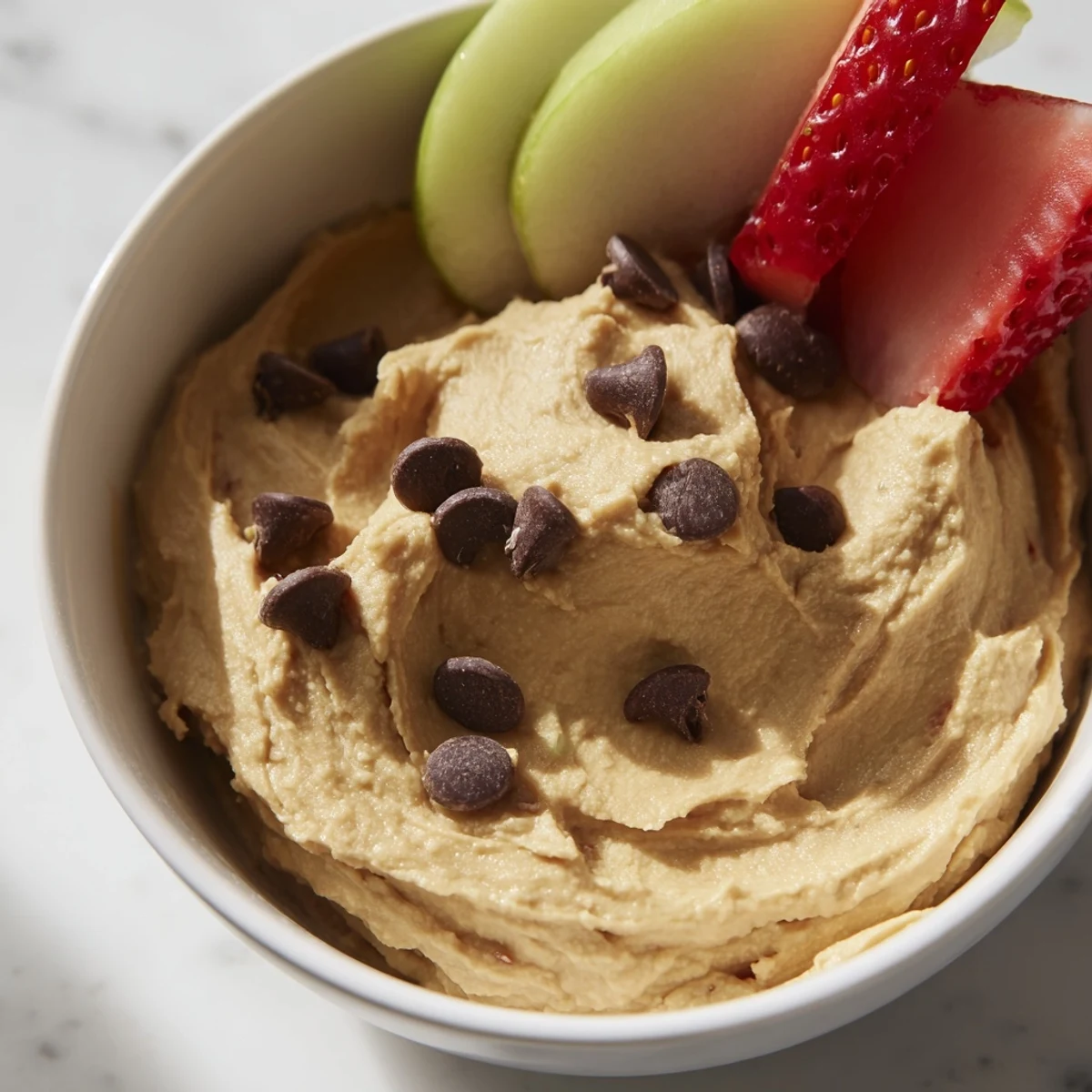Colorful fresh fruit platter with a creamy bowl of Chocolate Chip Cookie Dough Hummus for a healthy dessert snack.