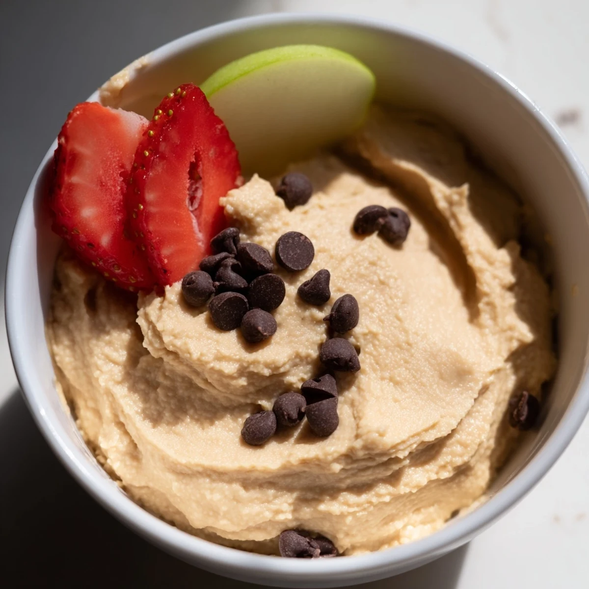 Close-up of Chocolate Chip Cookie Dough Hummus topped with mini chocolate chips, ready to serve with fruit.
