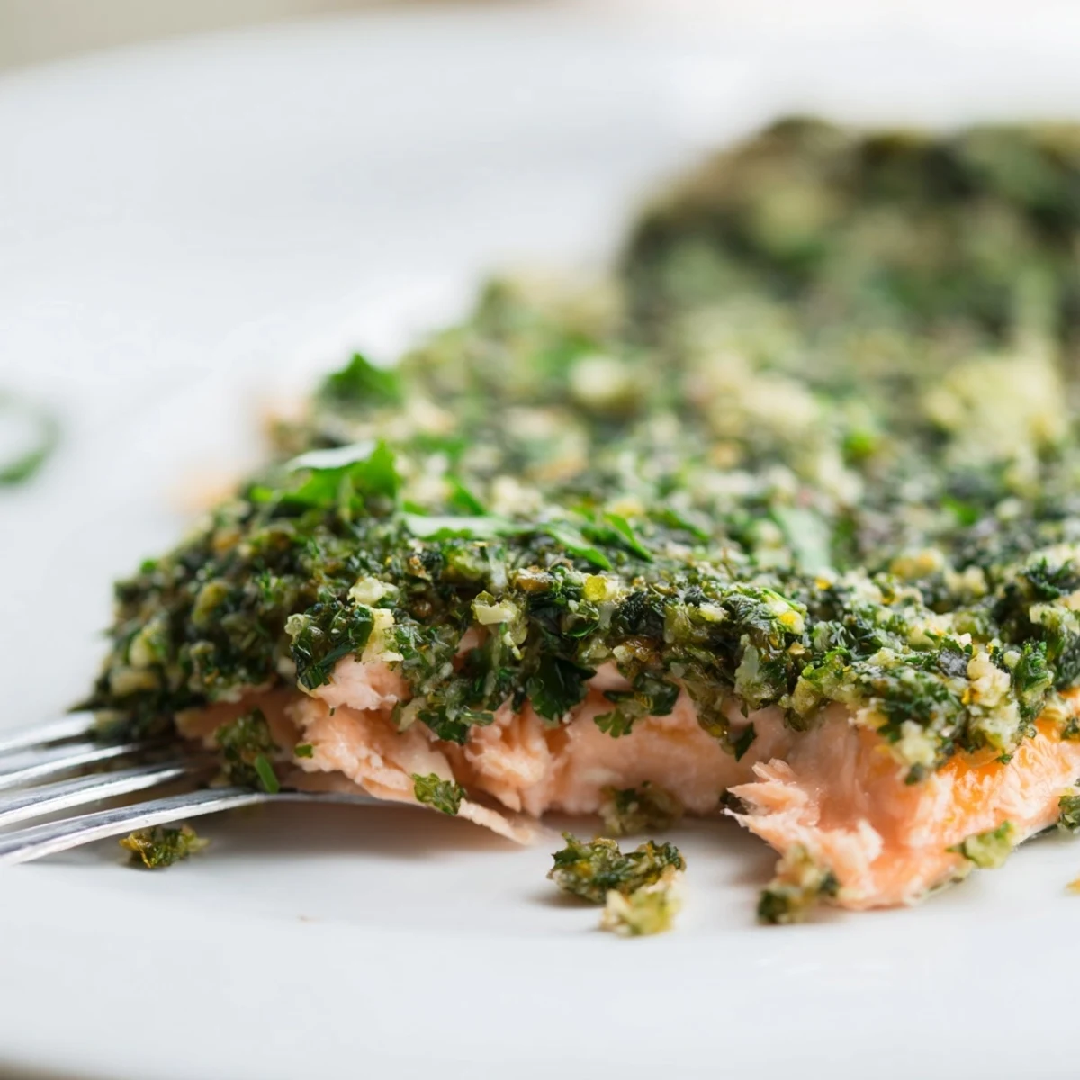 A close-up of tender flaky salmon, smothered in fresh parsley, basil, and caper salsa verde on a plate. 