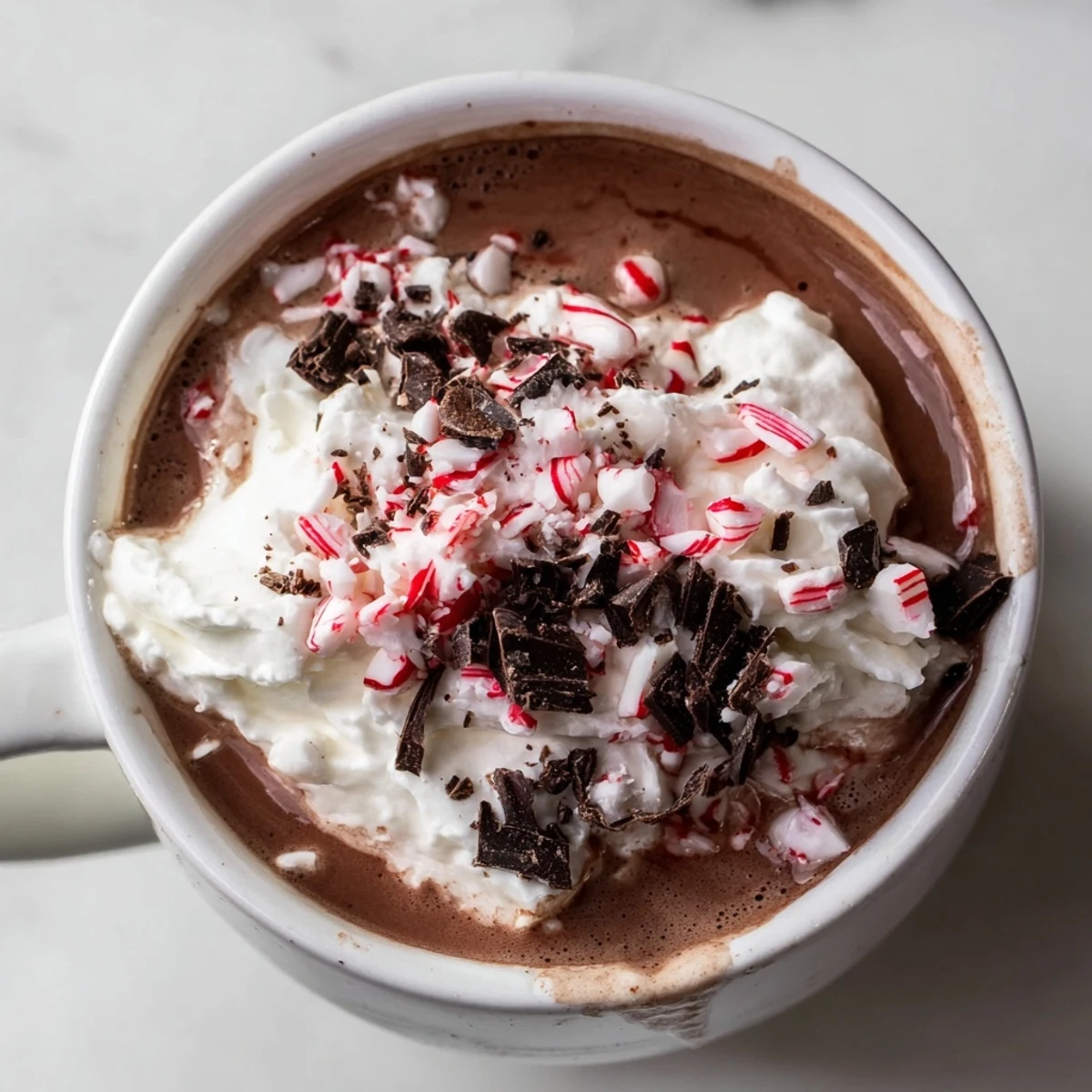 Frothy peppermint mocha hot chocolate steaming in a clear glass mug beside candy canes.