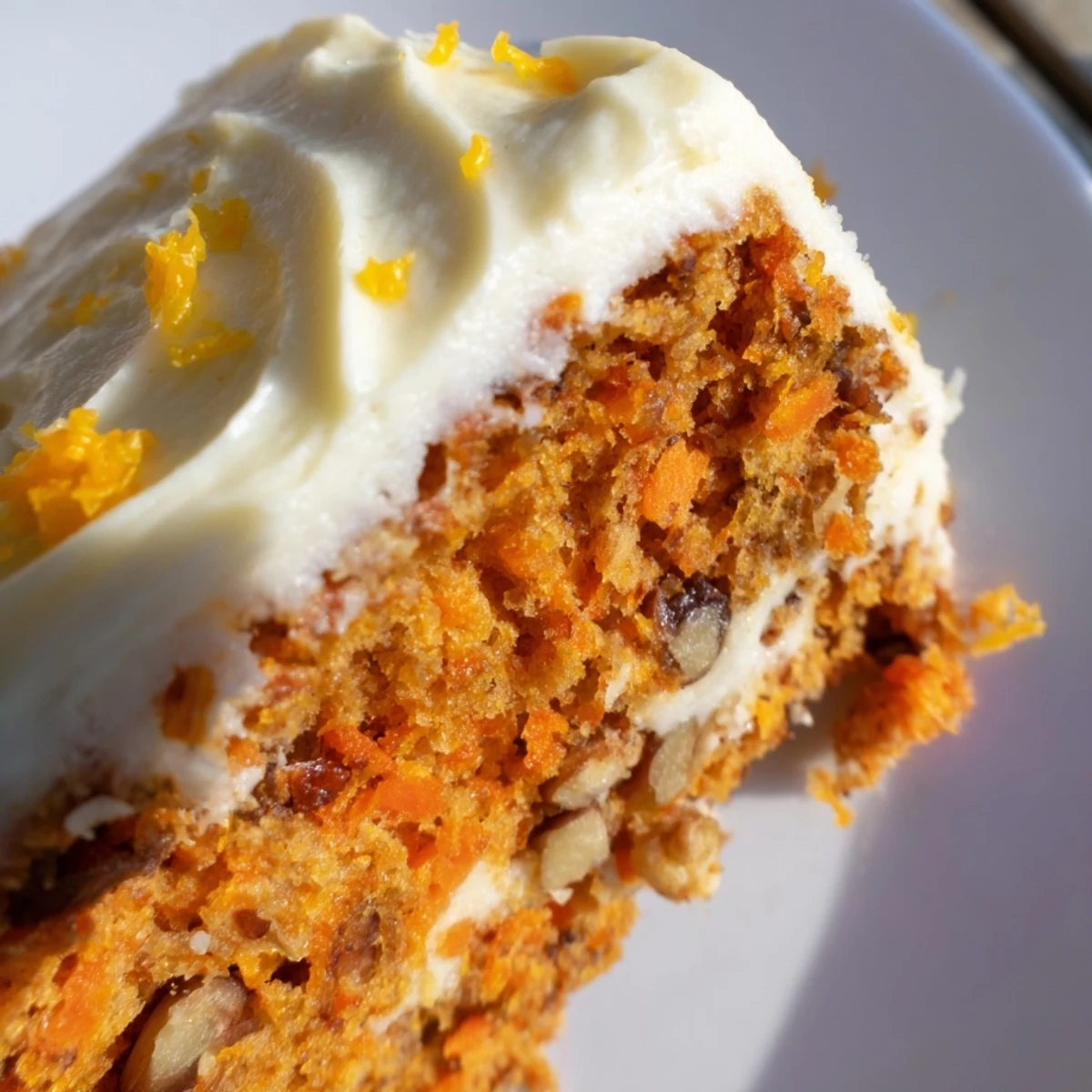 Freshly baked Spiced Carrot Cake with Orange Frosting on a wooden stand, garnished with zest and walnuts. 