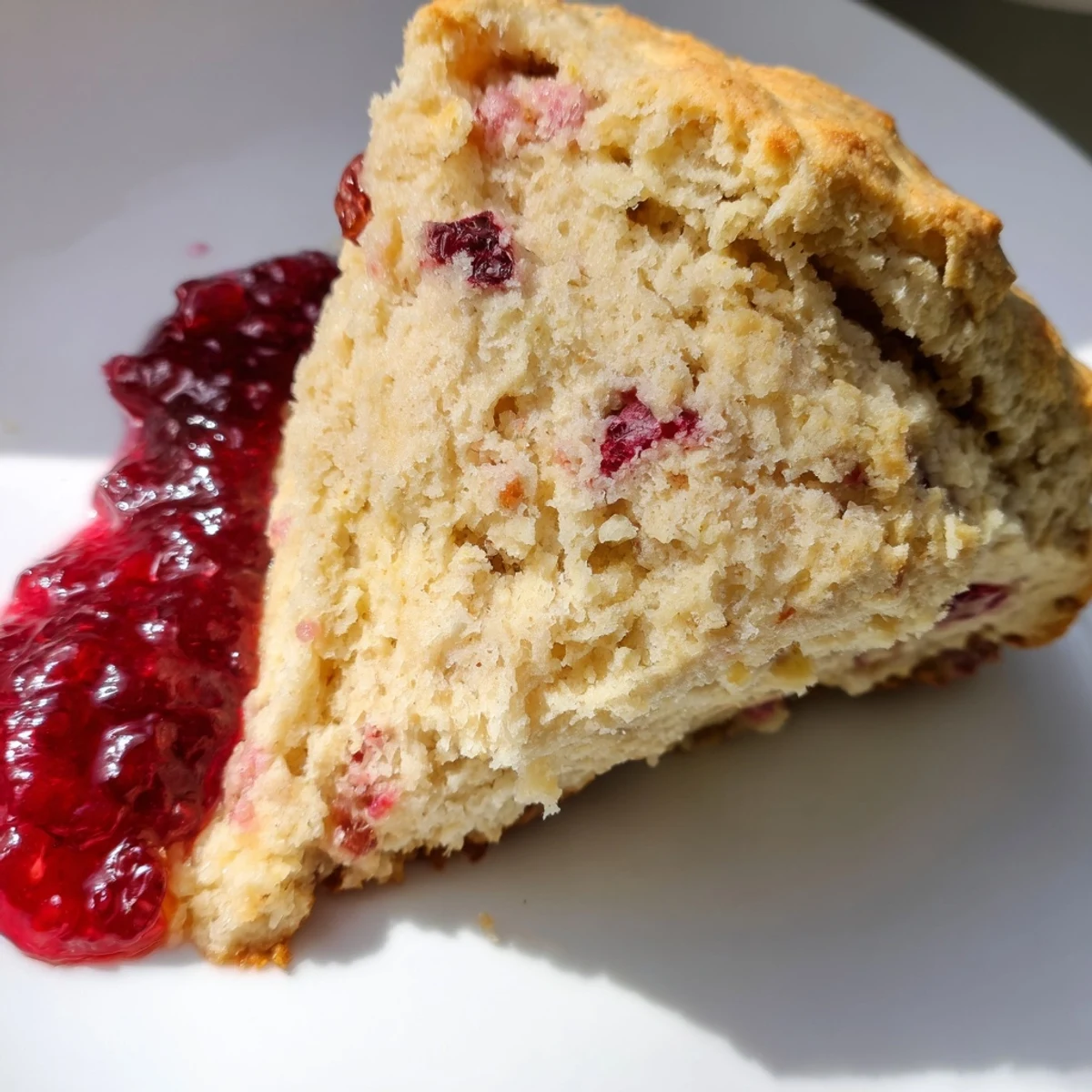 Homemade Cranberry Scone with Jam on a white plate with a jar of preserves, ready for afternoon tea.