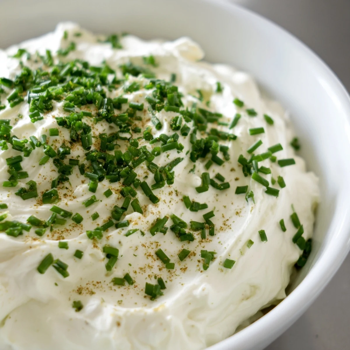 A chilled bowl of Creamy Snack Dip topped with fresh chives and parsley, ready for dipping.