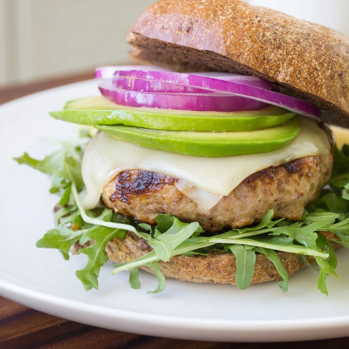 Toasted brioche bun holds a cooked turkey patty with Swiss cheese, avocado, red onion, and lettuce, served with sweet potato fries.