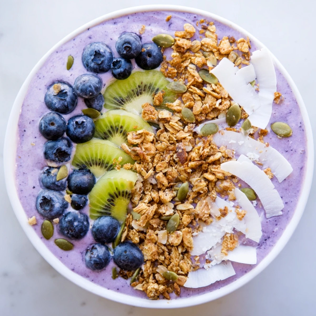 A vibrant Winter Berry Smoothie Bowl topped with crunchy granola, fresh kiwi slices, and bright red pomegranate seeds.