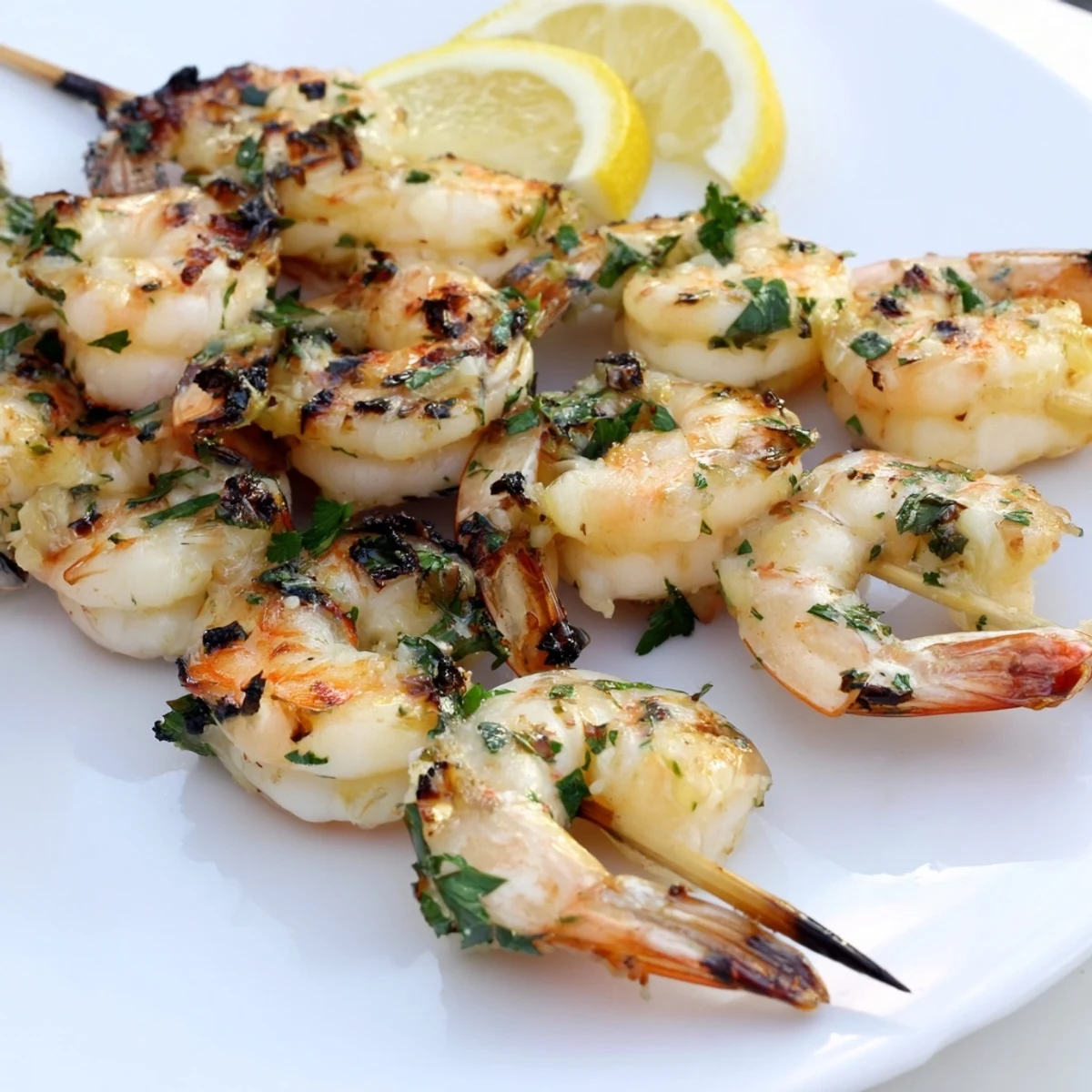 Juicy Lemon Garlic Shrimp Skewers grilled to charred perfection, glistening with olive oil and fresh herbs on a platter.