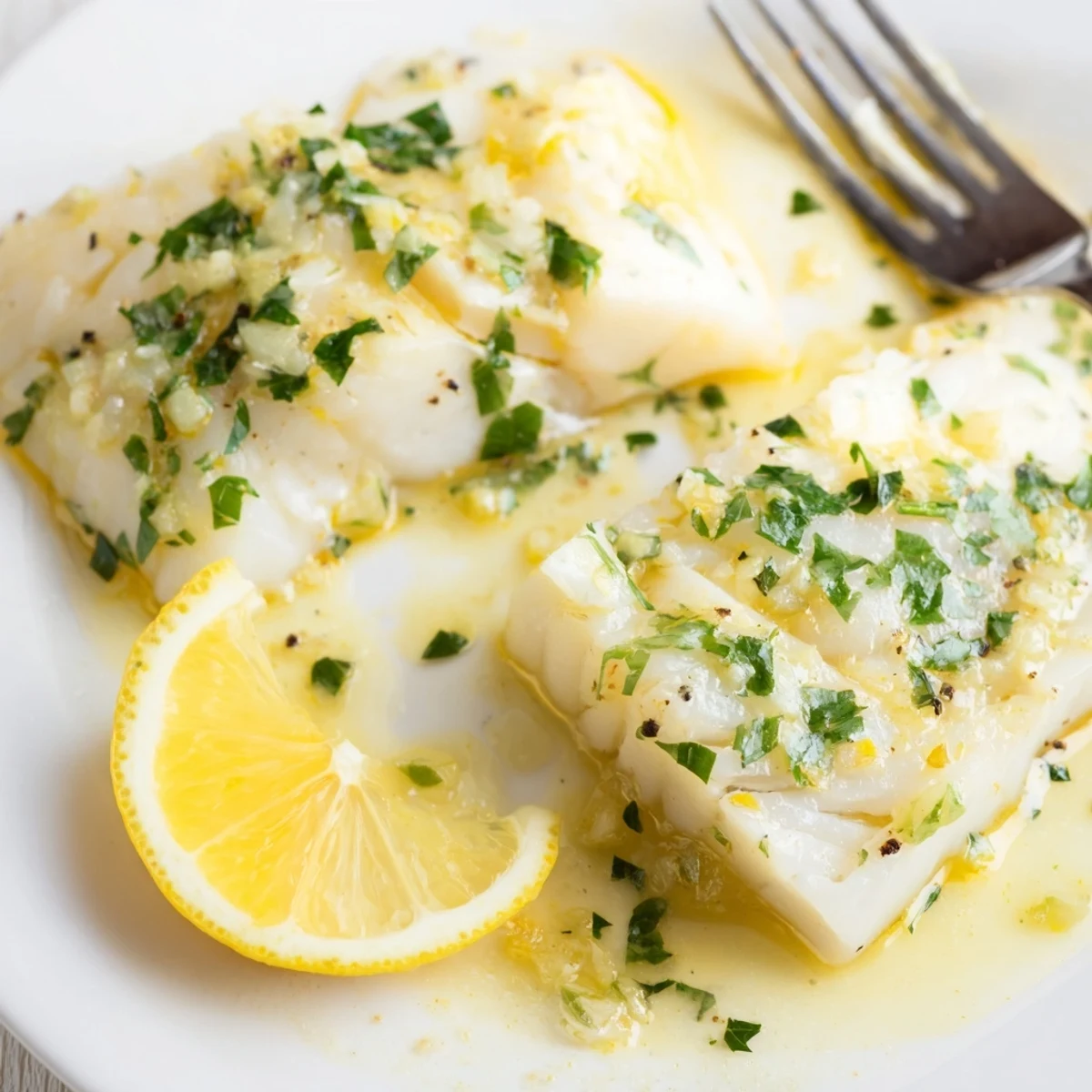 Flaky white fish on a dinner plate, drizzled with melted lemon butter sauce and garnished with chopped fresh parsley.