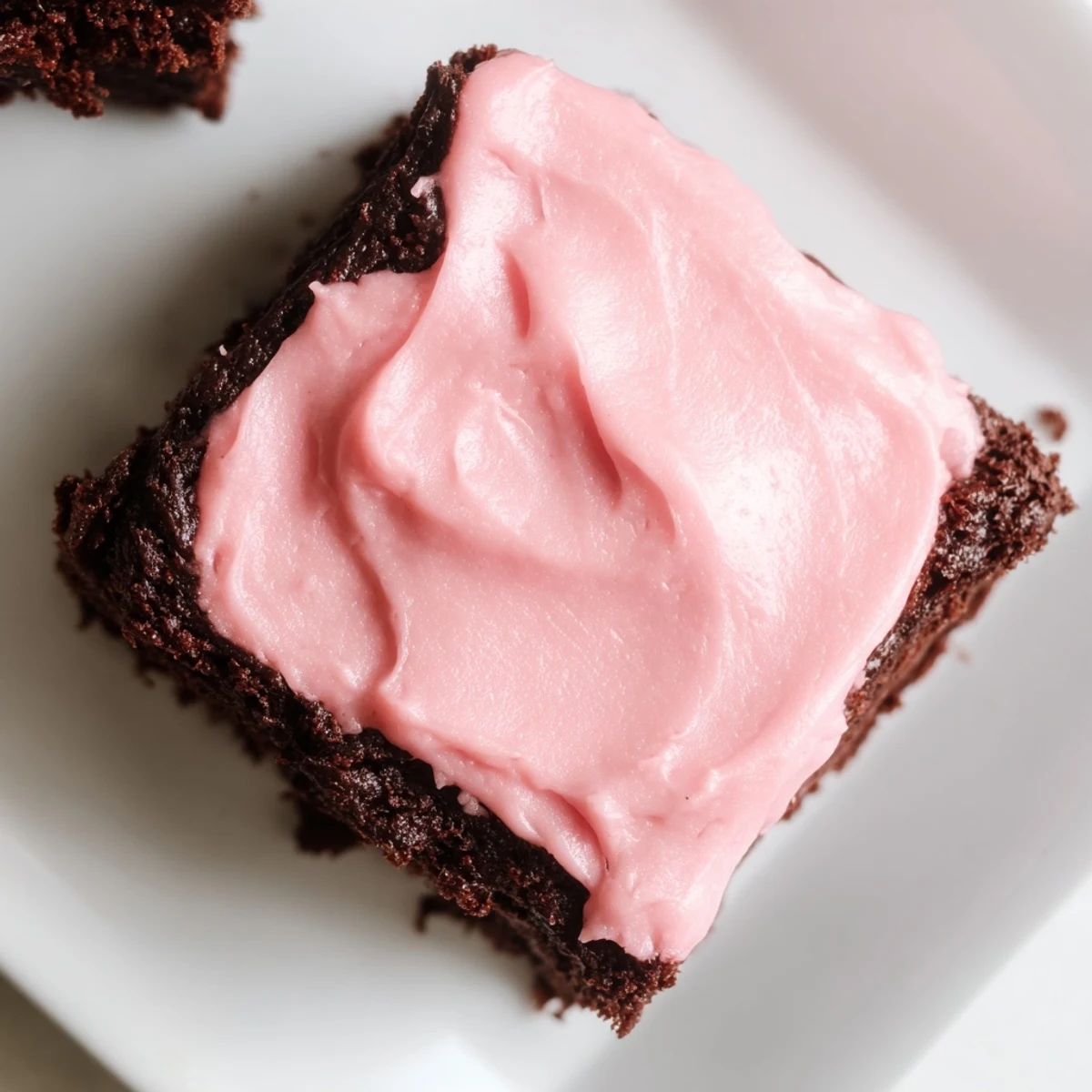 A close-up of pink frosted brownies highlights the creamy swirls and rich chocolate texture.