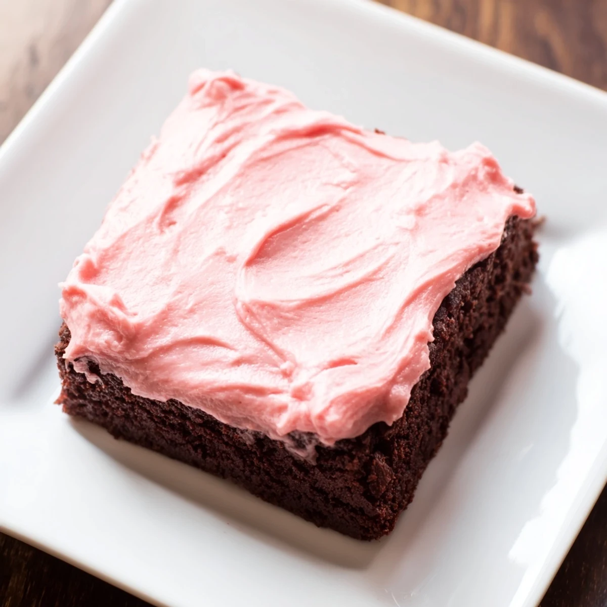 Stacked fudgy brownies topped with pink frosting offer a sweet treat for any occasion.