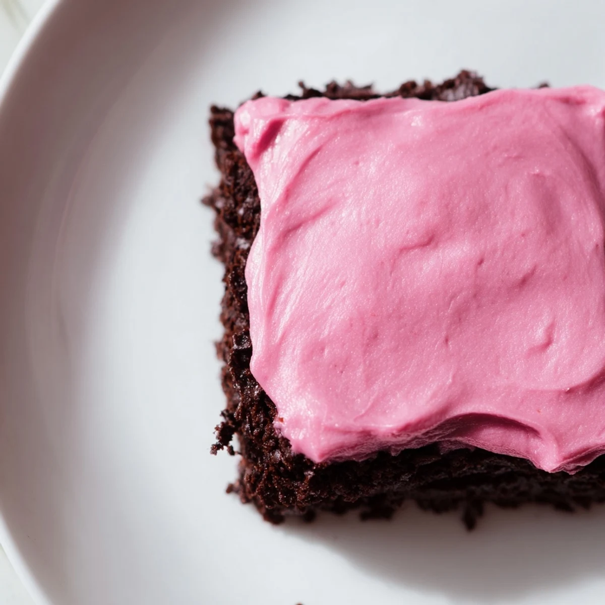 Freshly baked brownies with pink frosting, cut into squares on a marble counter, ready to serve.