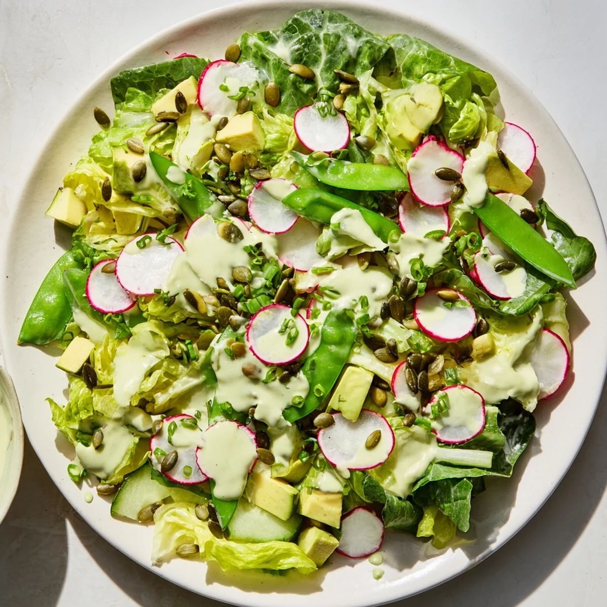 Creamy avocado chunks rest atop crunchy cucumbers and radishes in a Green Goddess Salad, drizzled with herby dressing.