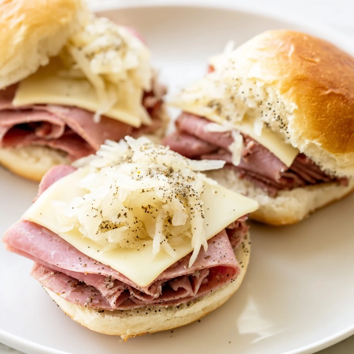 Golden Corned Beef Sliders with Mustard are arranged on a tray with melted Swiss cheese and poppy seeds.