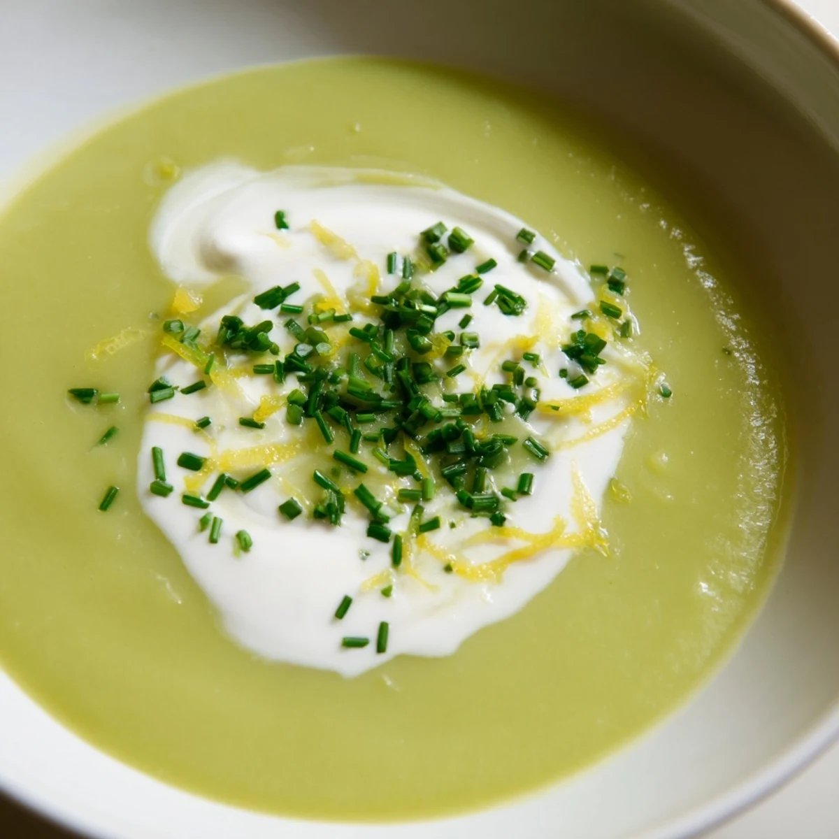Creamy Asparagus Soup with Lemon is a vibrant green soup served steaming in a white bowl with a lemon wedge.
