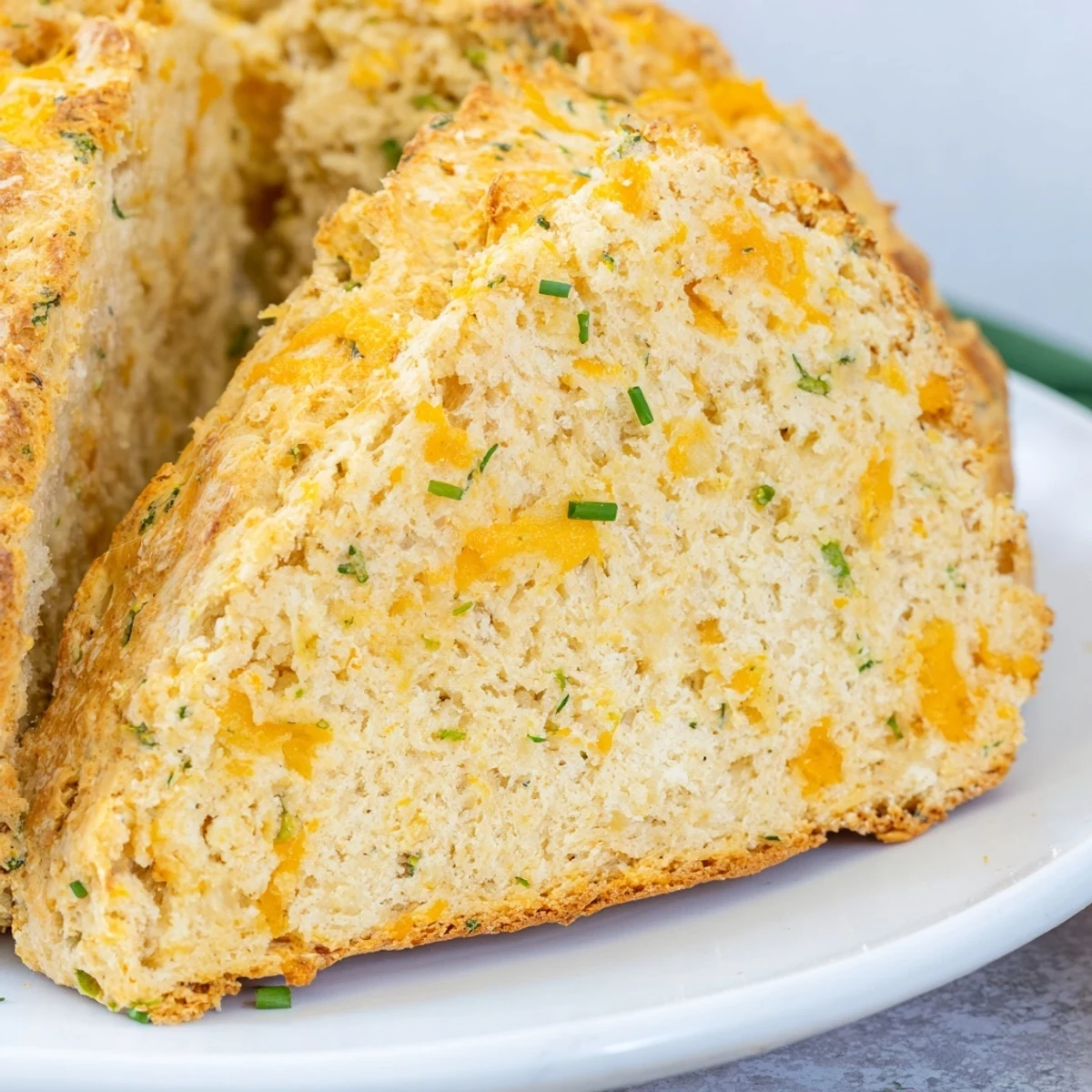 Warm slices of Savory Cheddar & Chive Irish Soda Bread on a plate, perfect with a steaming bowl of tomato soup for a cozy lunch.