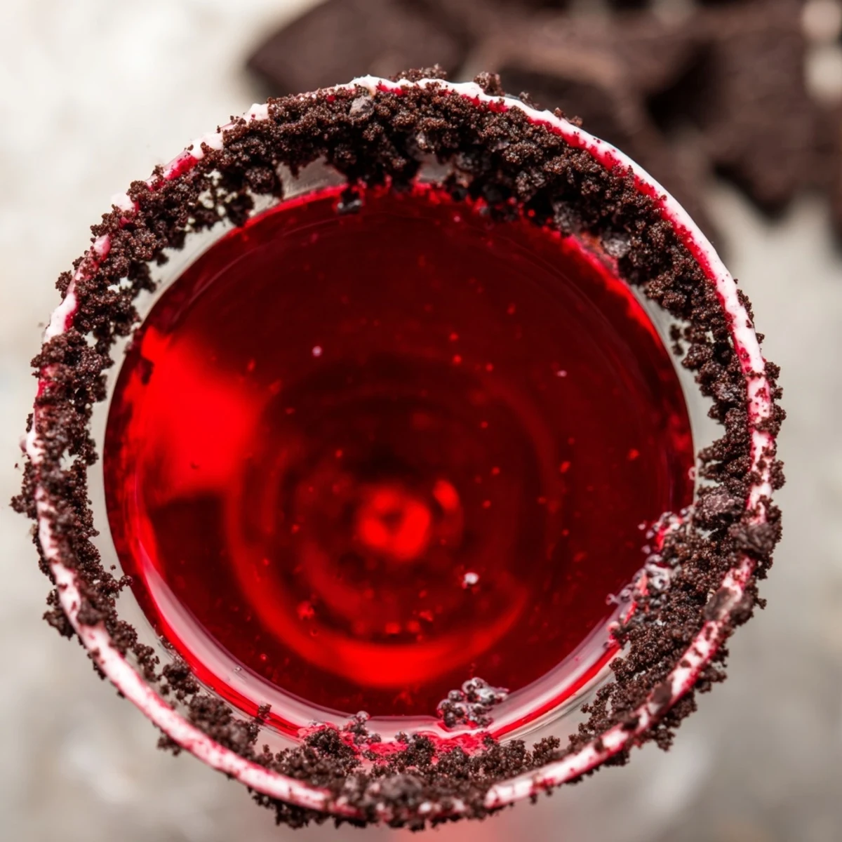 Two chilled Decadent Red Velvet Martinis sit on a marble counter, rimmed with cream cheese frosting and topped with chocolate shavings.
