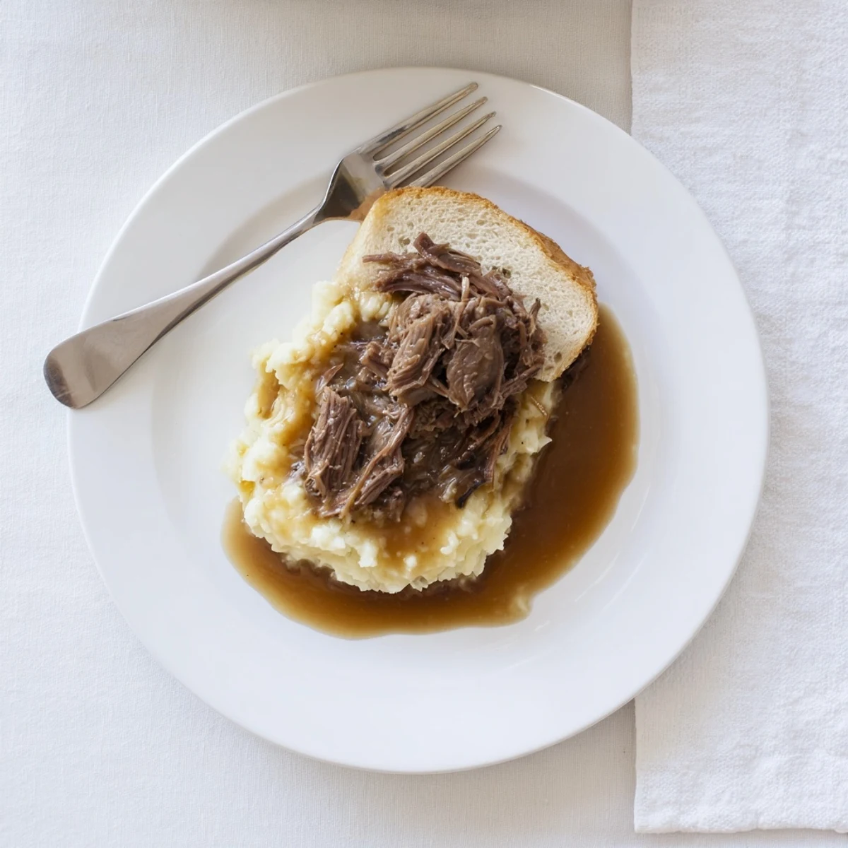 Golden brown gravy ladled over Slow Cooker Beef Manhattan with fluffy mashed potatoes and thick Texas toast on a rustic plate.