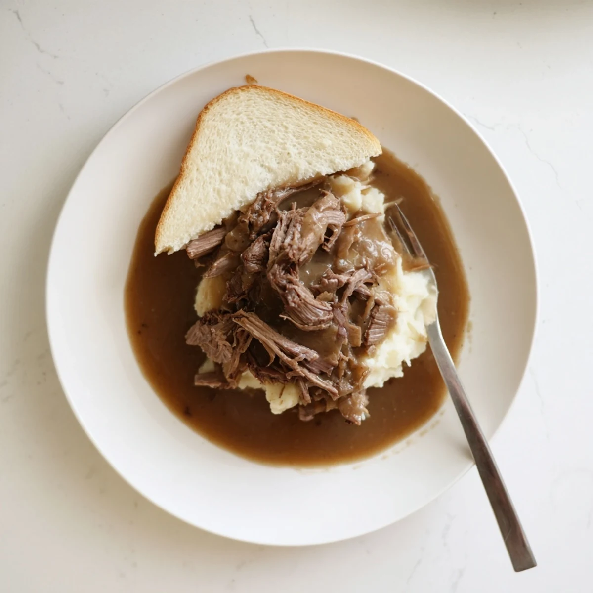 Slow Cooker Beef Manhattan features tender shredded beef and creamy mashed potatoes on thick white bread, drizzled with rich brown gravy.