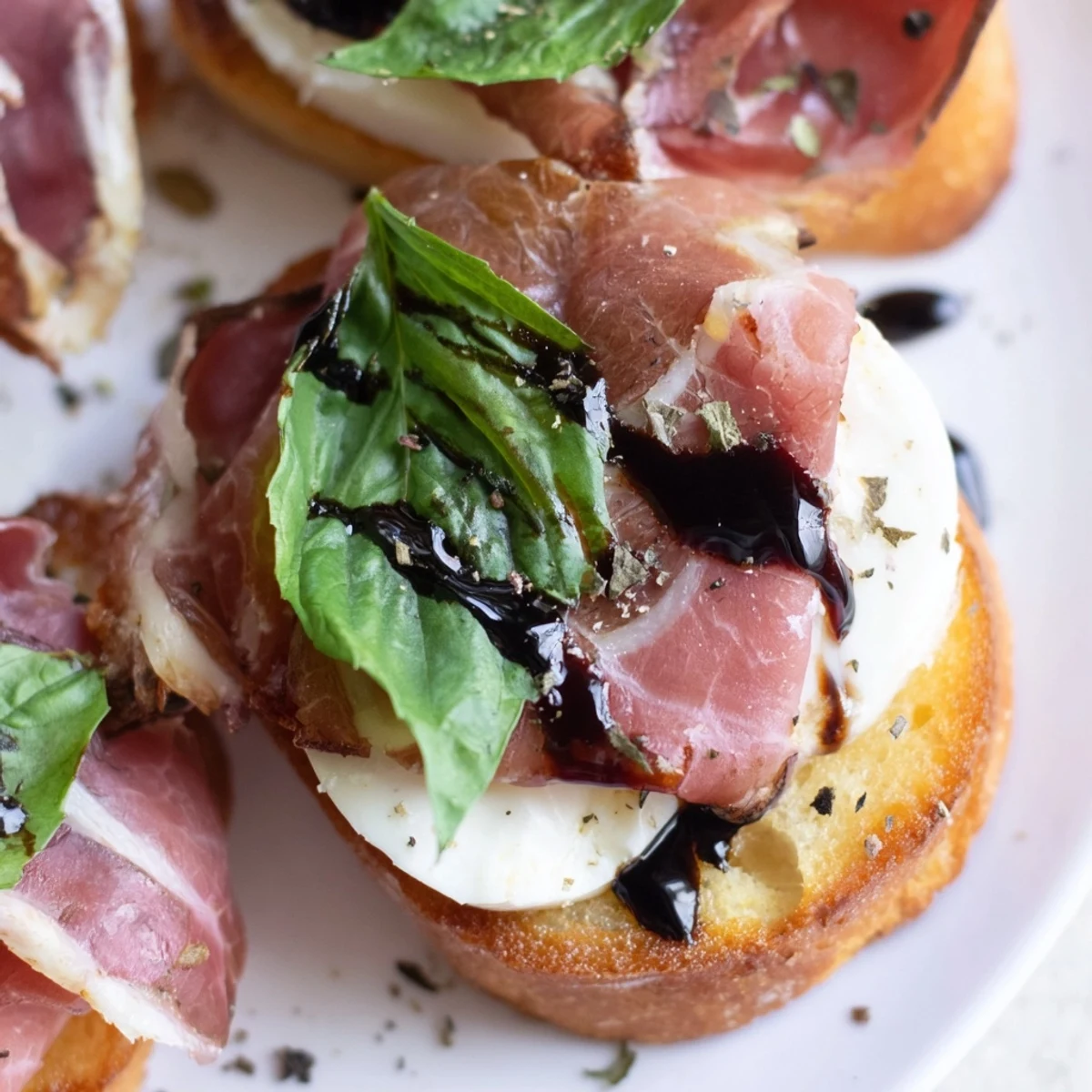 A stack of warm Mozzarella Beef Prosciutto Crostini with glistening balsamic glaze, ideal for serving at a dinner party or family gathering.