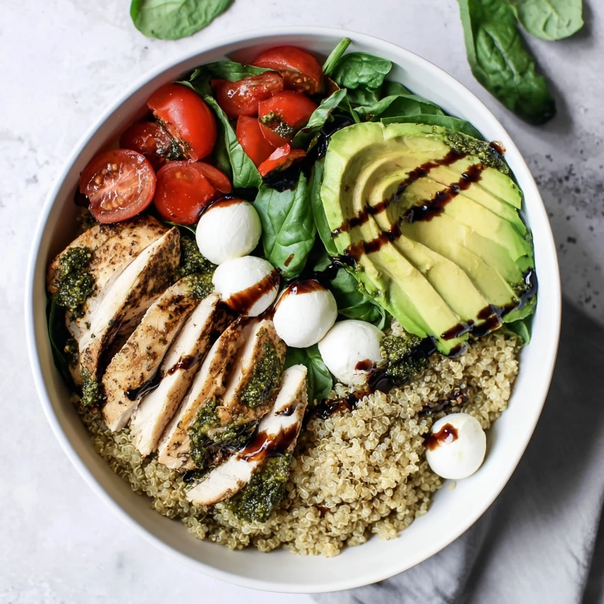 The vibrant Pesto Chicken Caprese Grain Bowl features juicy sliced chicken atop quinoa, tomatoes, and mozzarella.