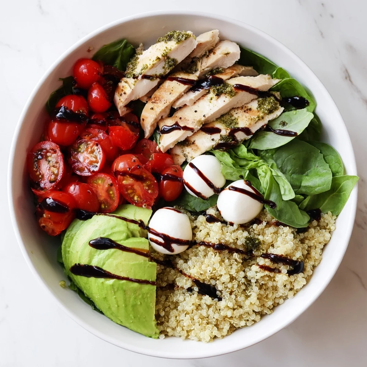 Savor this Pesto Chicken Caprese Grain Bowl with fresh basil and balsamic drizzle over greens and avocado.