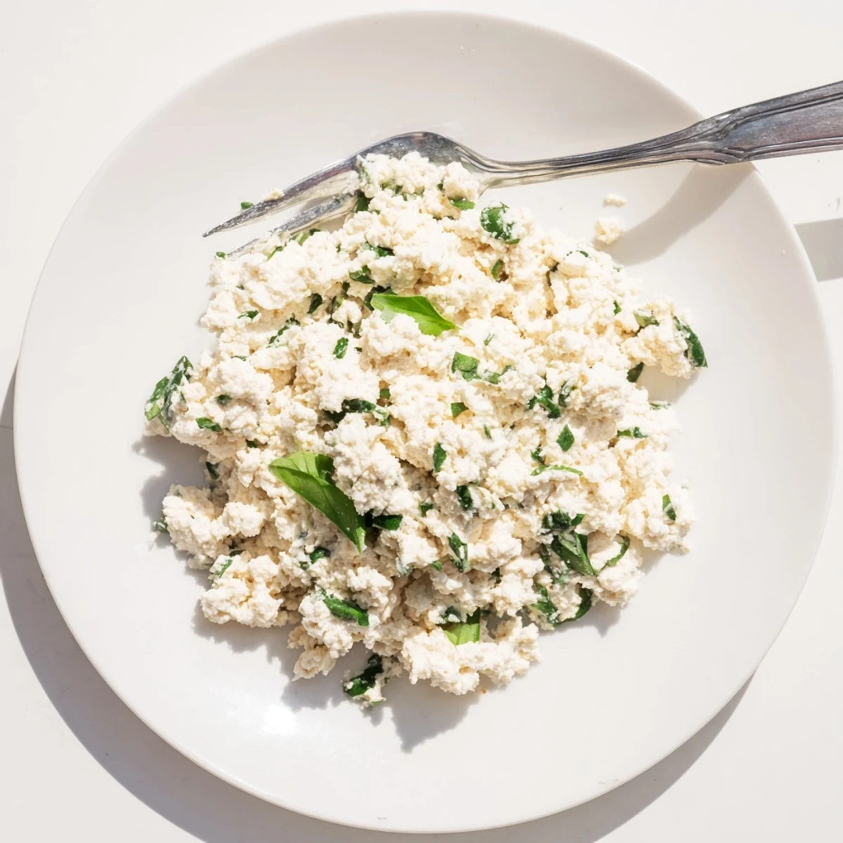 Tofu Ricotta being spooned into a baking dish for a dairy-free lasagna, garnished with lemon zest and herbs.