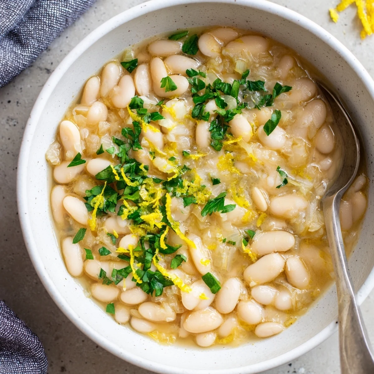 Creamy white Miso Butter Brothy Beans simmered in a fragrant savory broth, topped with fresh herbs and a bright lemon zest garnish.