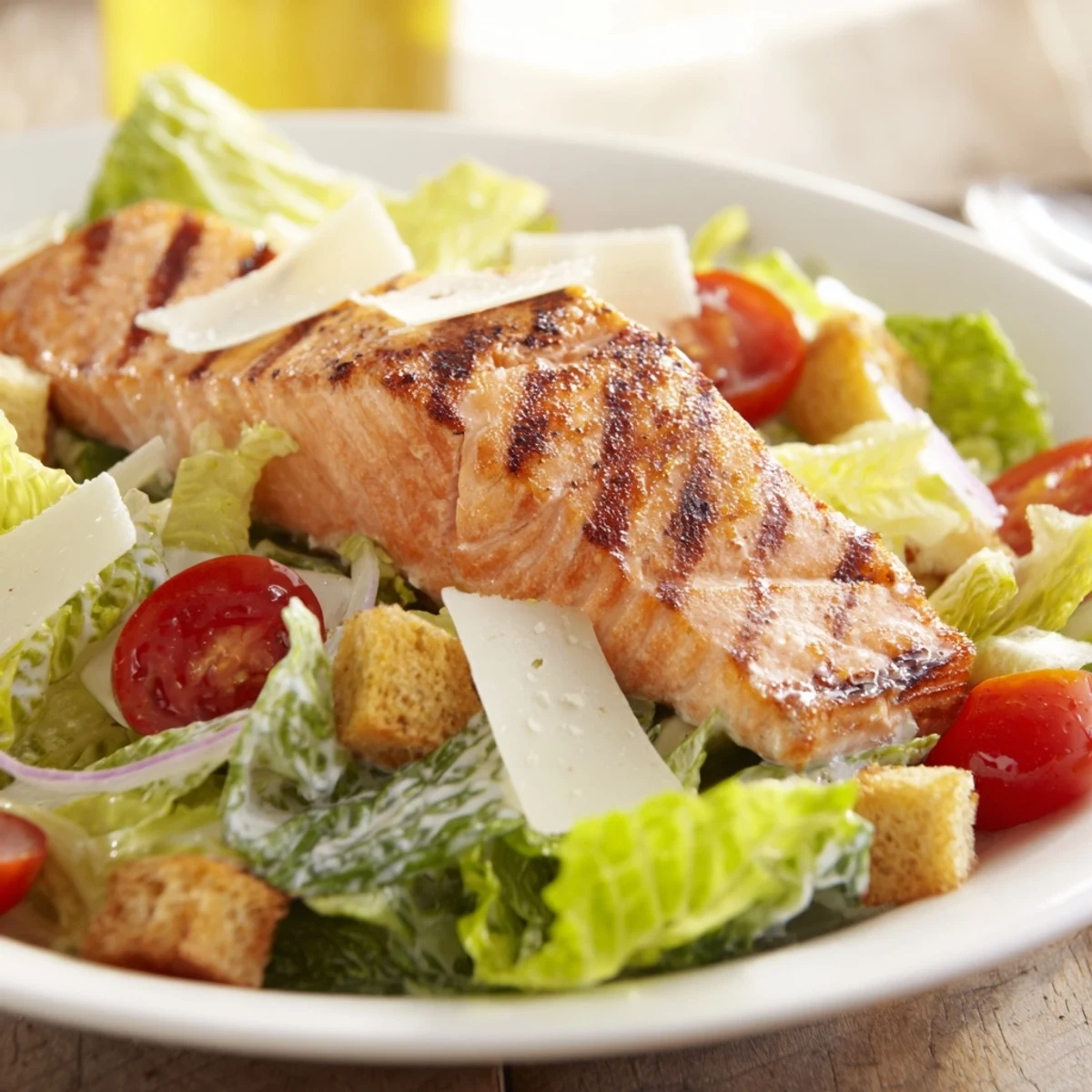 A close-up of Salmon Caesar Salad with grilled salmon, crisp romaine, and crunchy croutons topped with creamy dressing.