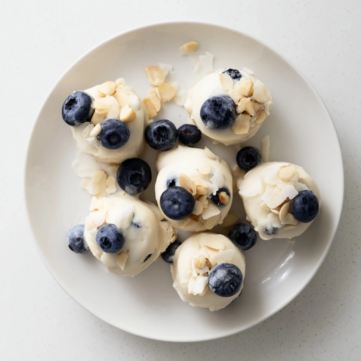 Close-up of creamy blueberry Greek yogurt bites with indigo fruit centers dusted with shredded coconut and ready for freezing