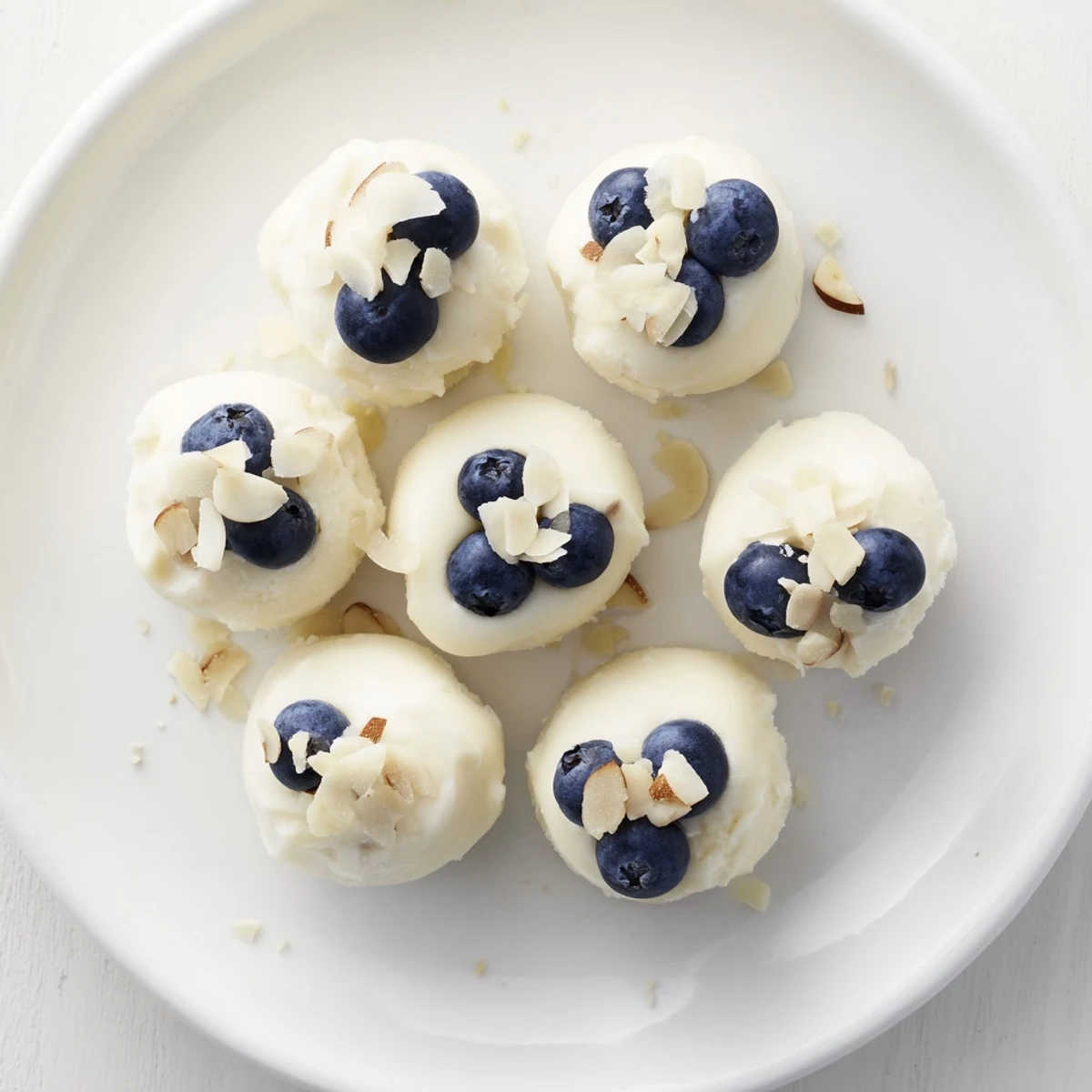 Frozen blueberry Greek yogurt bites topped with chopped almonds and coconut flakes on a white serving plate for healthy snacking