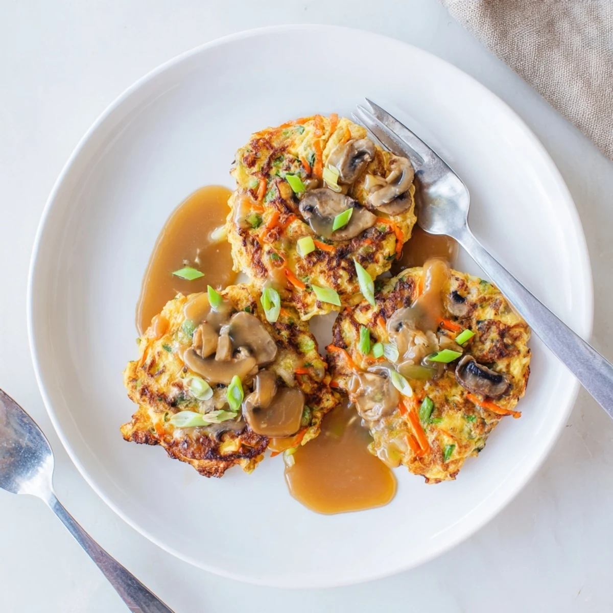 Golden brown crispy Egg Foo Young patties drizzled with savory brown gravy on white plate