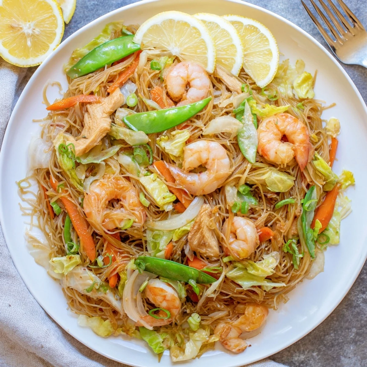Steamy plate of traditional Pancit Bihon featuring tender rice noodles with chicken, shrimp, and colorful vegetables