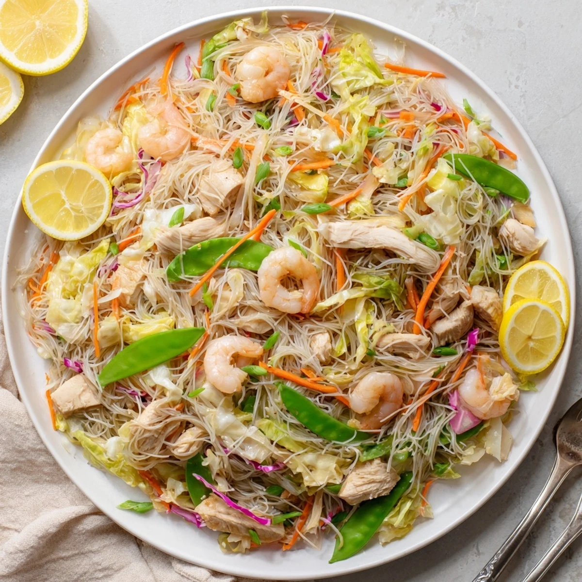 Homemade Pancit Bihon garnished with fresh scallions and served with bright citrus wedges for a complete Filipino meal