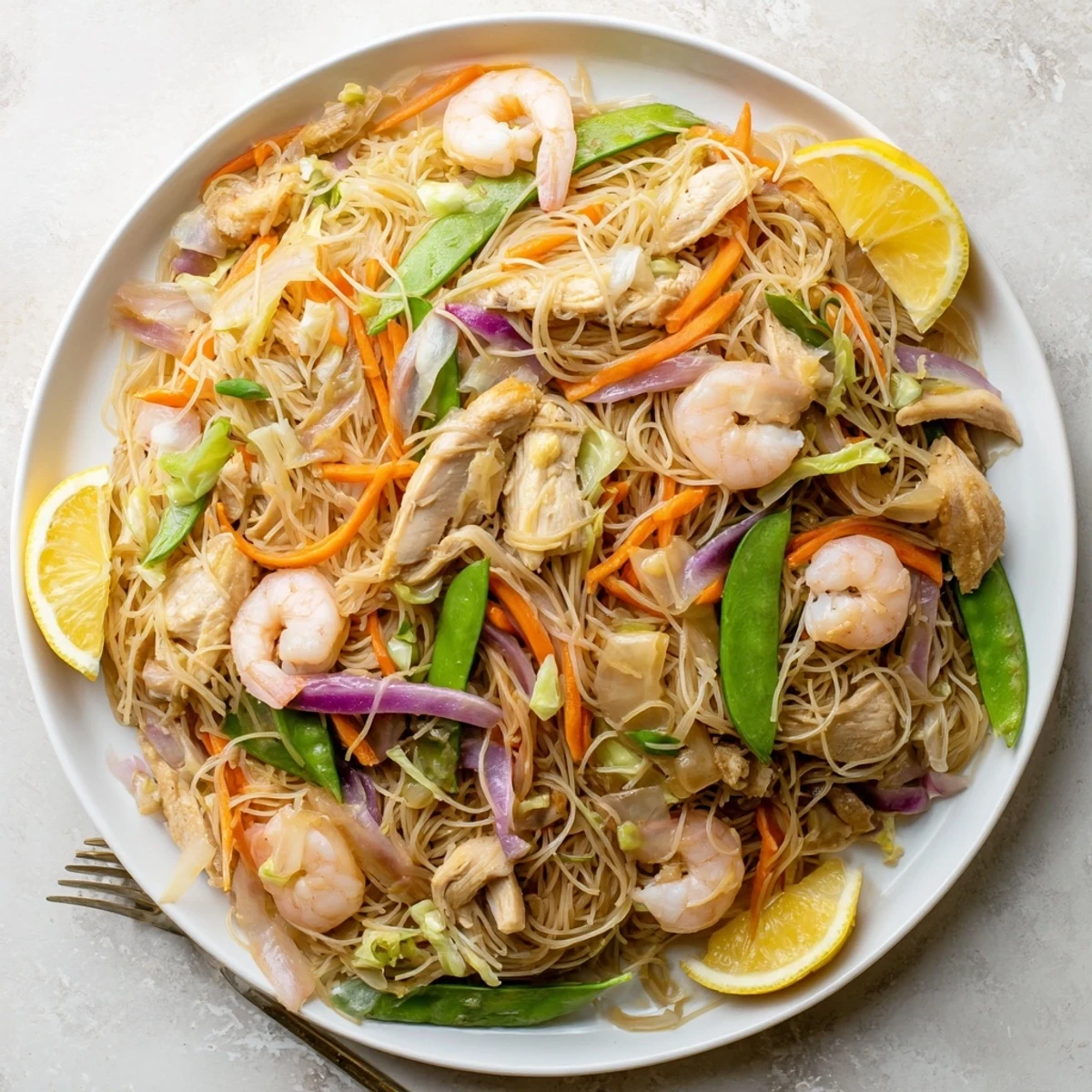 Golden stir-fried Pancit Bihon noodles tossed with juicy shrimp, sliced chicken, and crisp carrot and cabbage strips