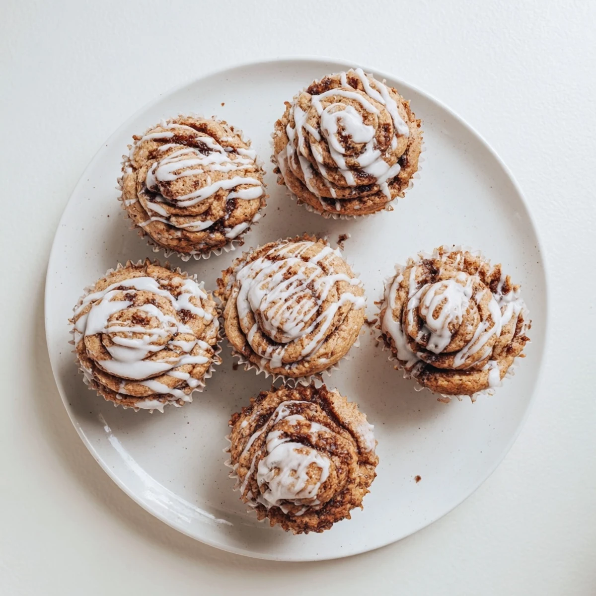 Golden cinnamon roll protein muffins topped with sweet vanilla drizzle on a white plate