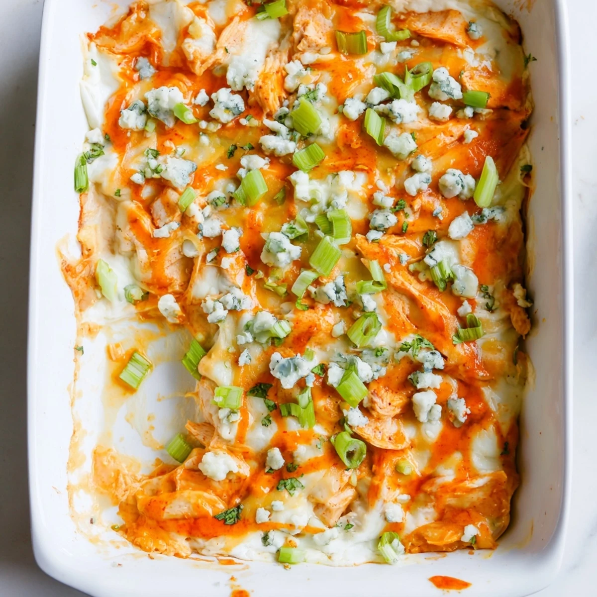 Creamy buffalo chicken casserole with shredded cheese and green onion garnish on white plate