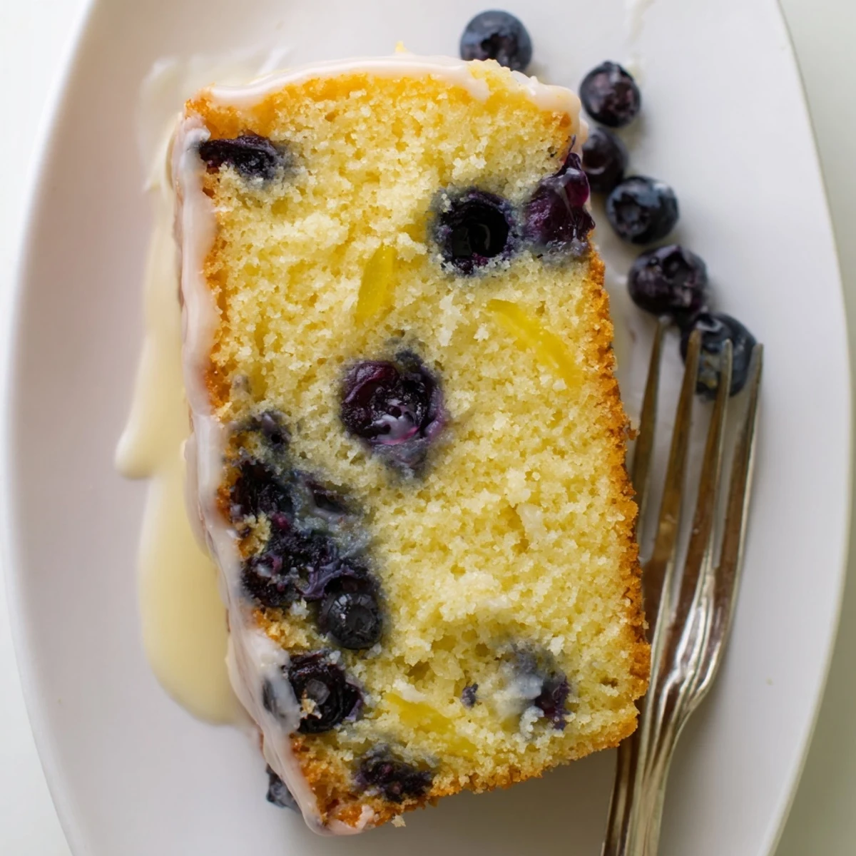 Golden slice of lemon blueberry cake with zesty glaze on a white serving plate