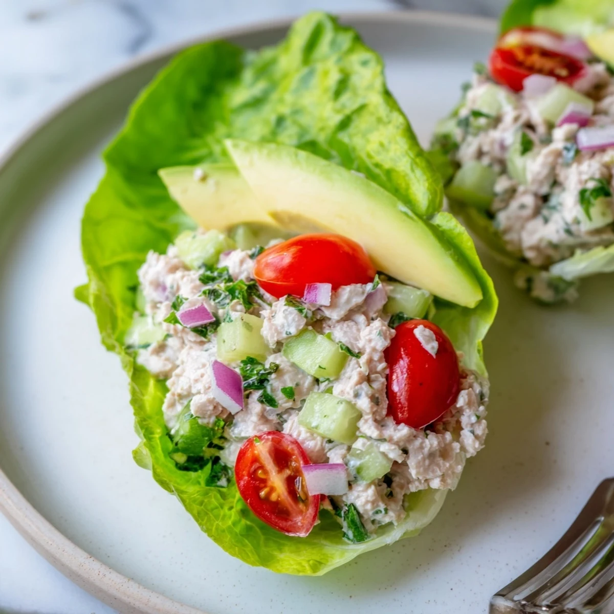 Low-carb tuna salad lettuce wraps topped with avocado slices and ripe cherry tomatoes