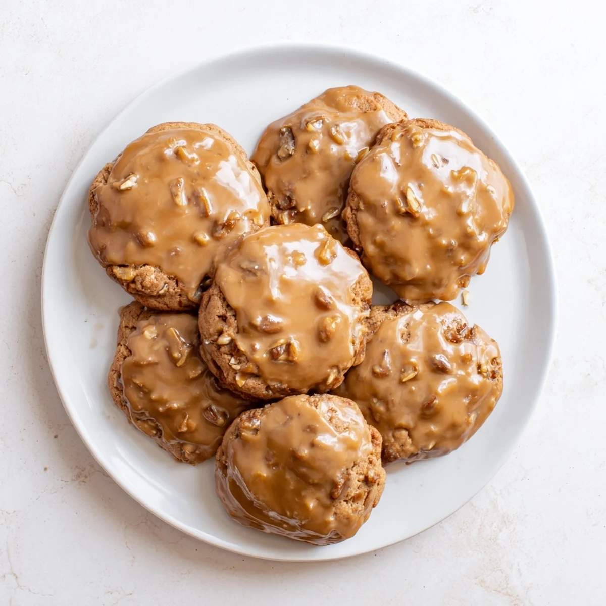 Freshly baked sticky toffee pudding cookies stacked high with dripping caramel toffee glaze and visible date pieces