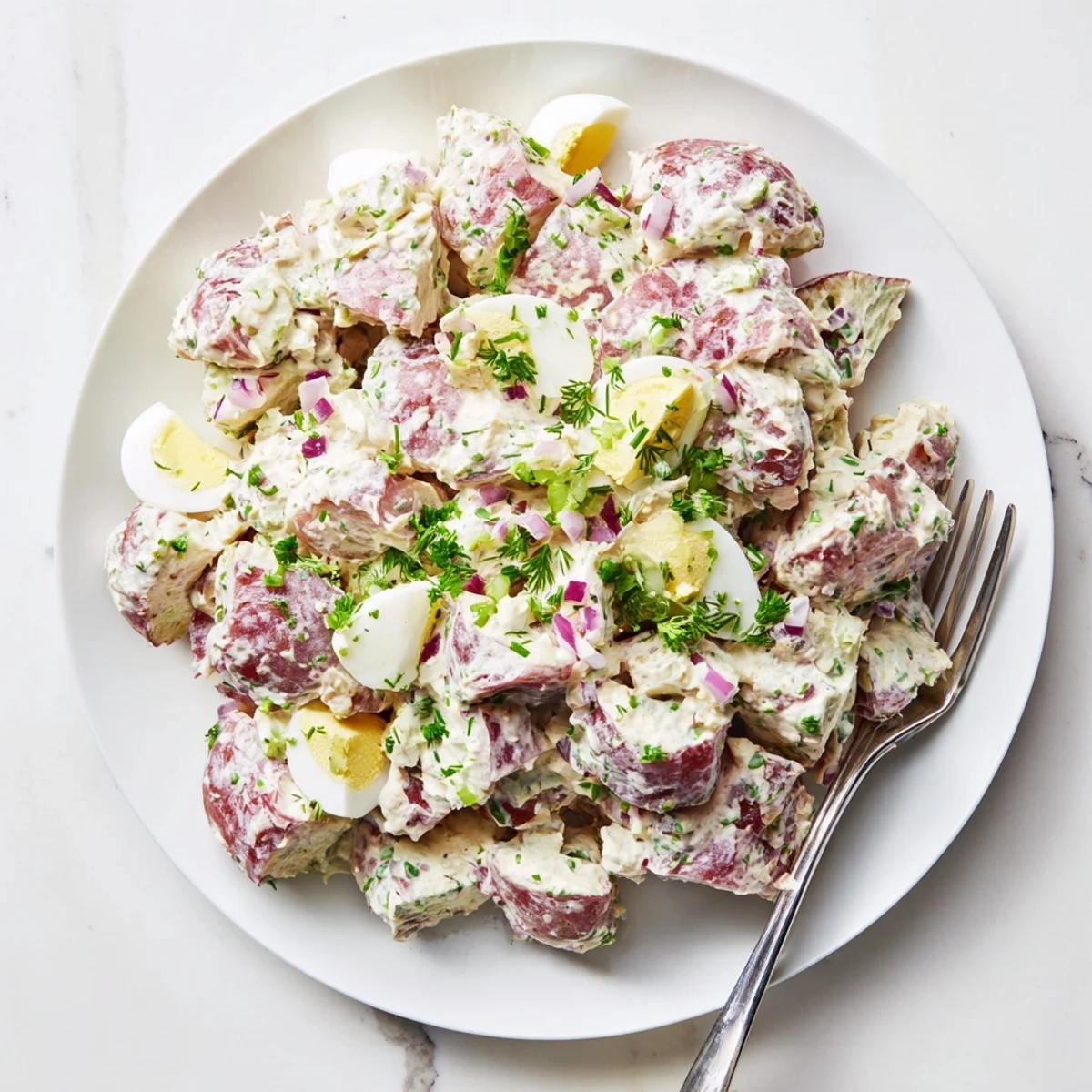 Classic American red potato salad featuring hard-boiled eggs and creamy dressing on a white platter