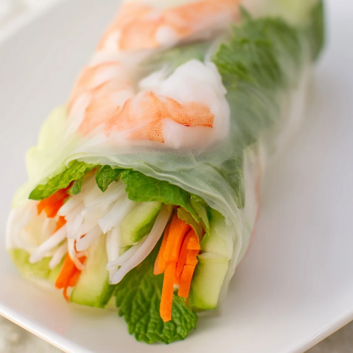 Vietnamese-style fresh spring rolls with peanut sauce displaying crisp julienned carrots, cucumber, and herbs through the delicate wrapper