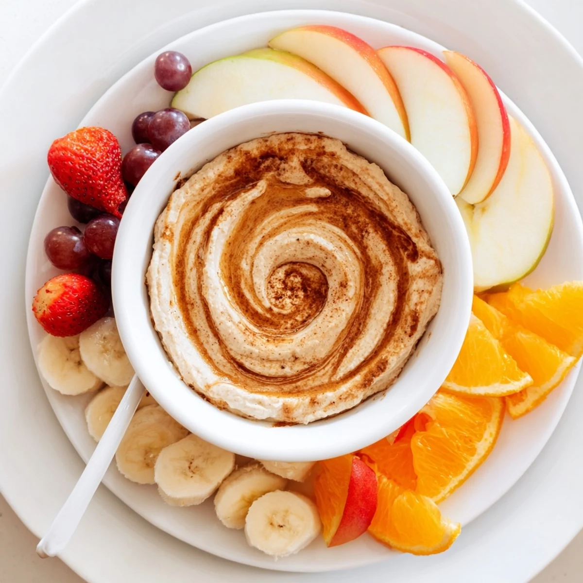 Creamy healthy Greek yogurt cinnamon roll dip swirled with cinnamon and served with fresh sliced apples and strawberries on a wooden platter