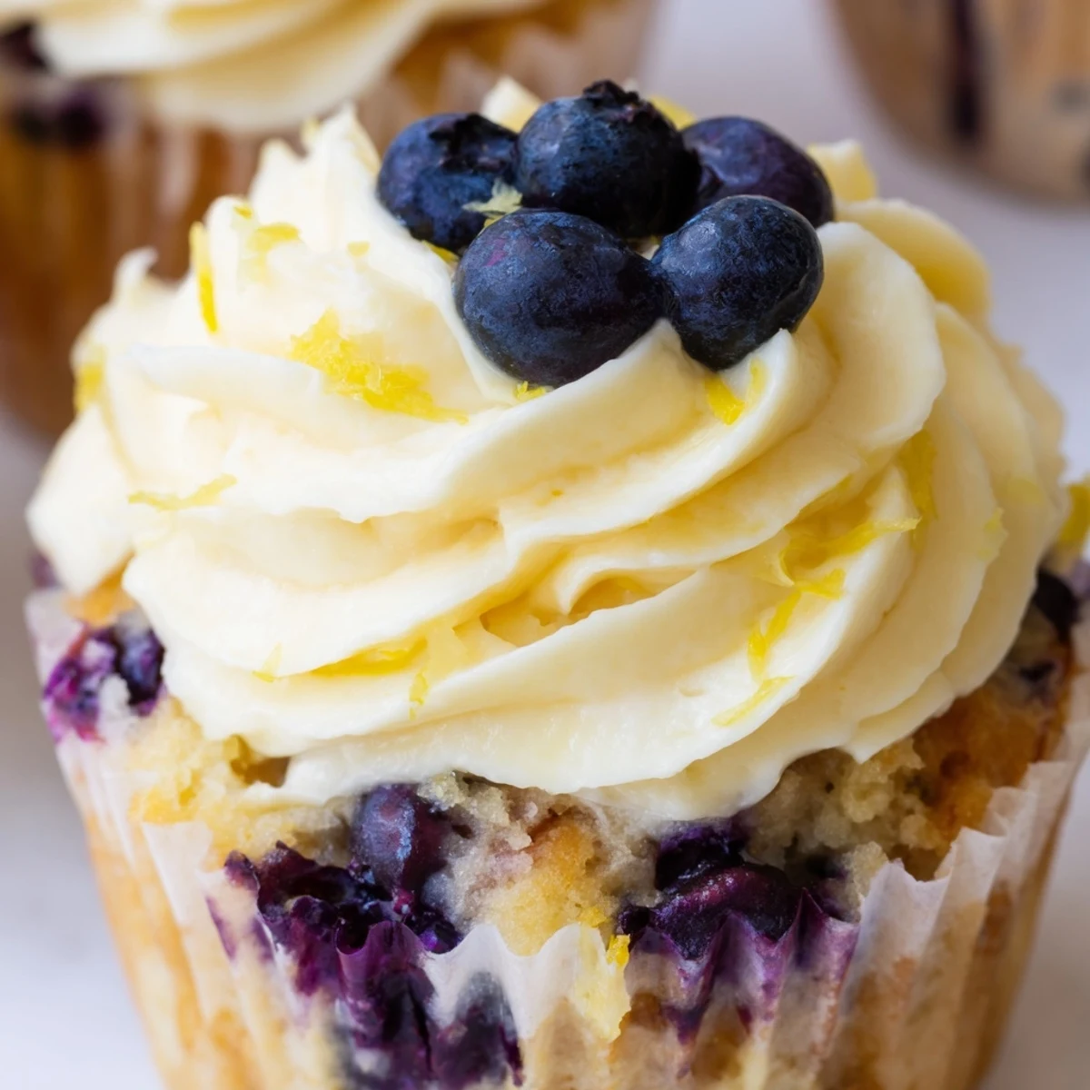 Golden lemon blueberry cupcakes topped with swirls of tangy cream cheese frosting and fresh blueberry garnish