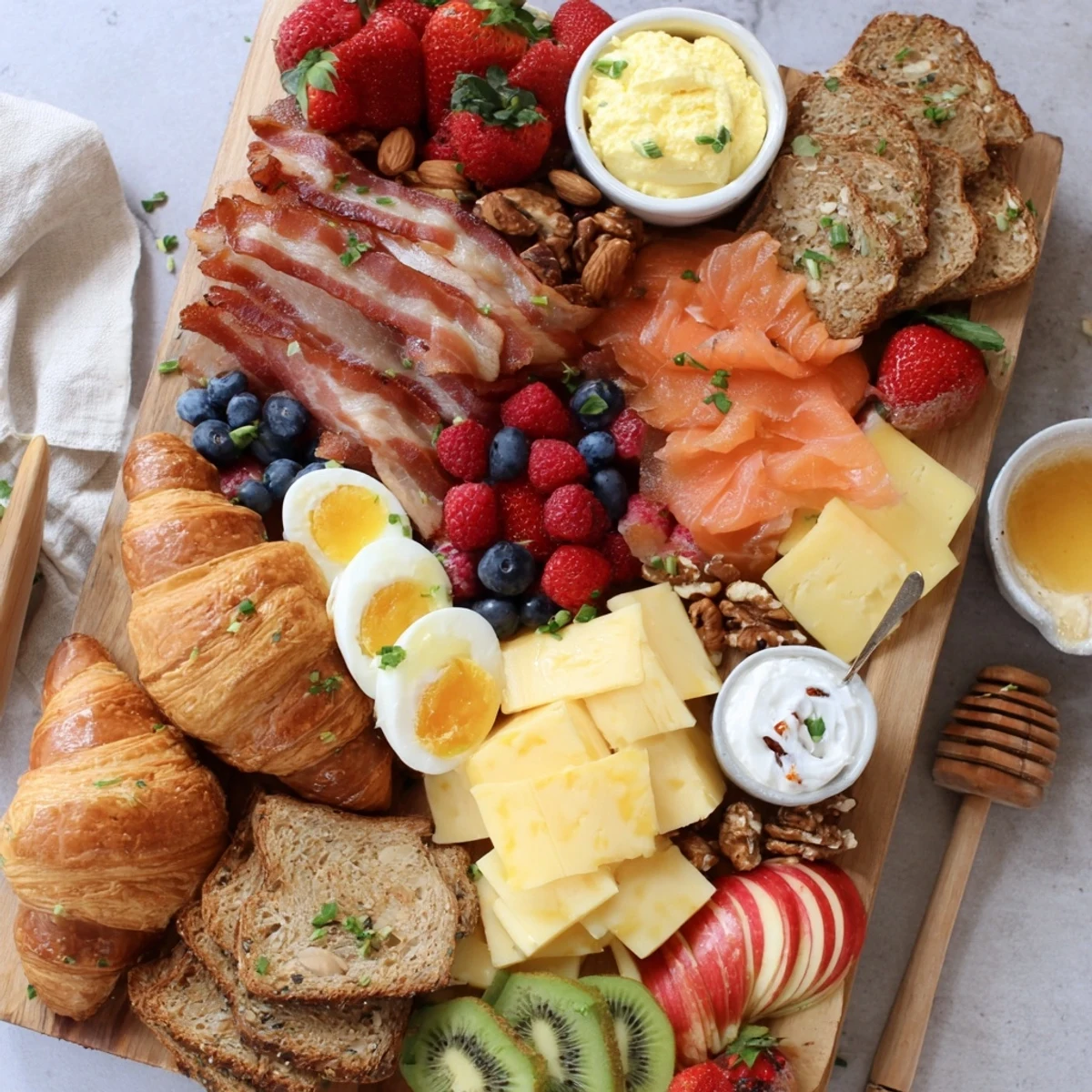 Decorative breakfast charcuterie board displaying bacon, cheddar, boiled eggs, and toasted bagels with colorful fruit garnishes