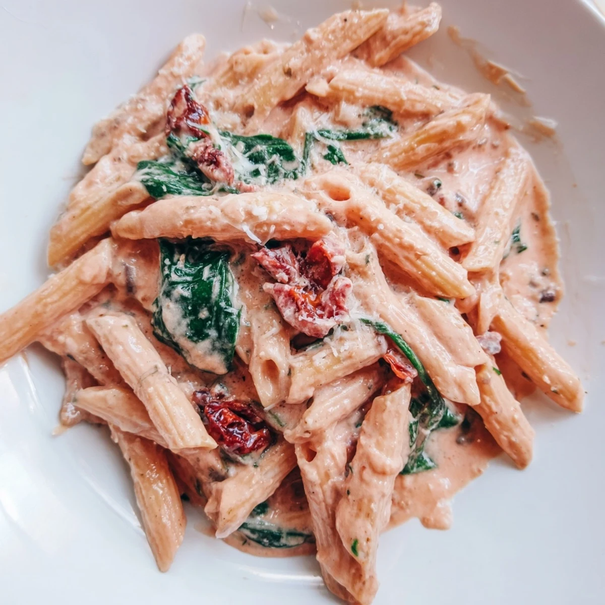 Creamy sun dried tomato spinach pasta in a rustic skillet with vibrant green wilted leaves