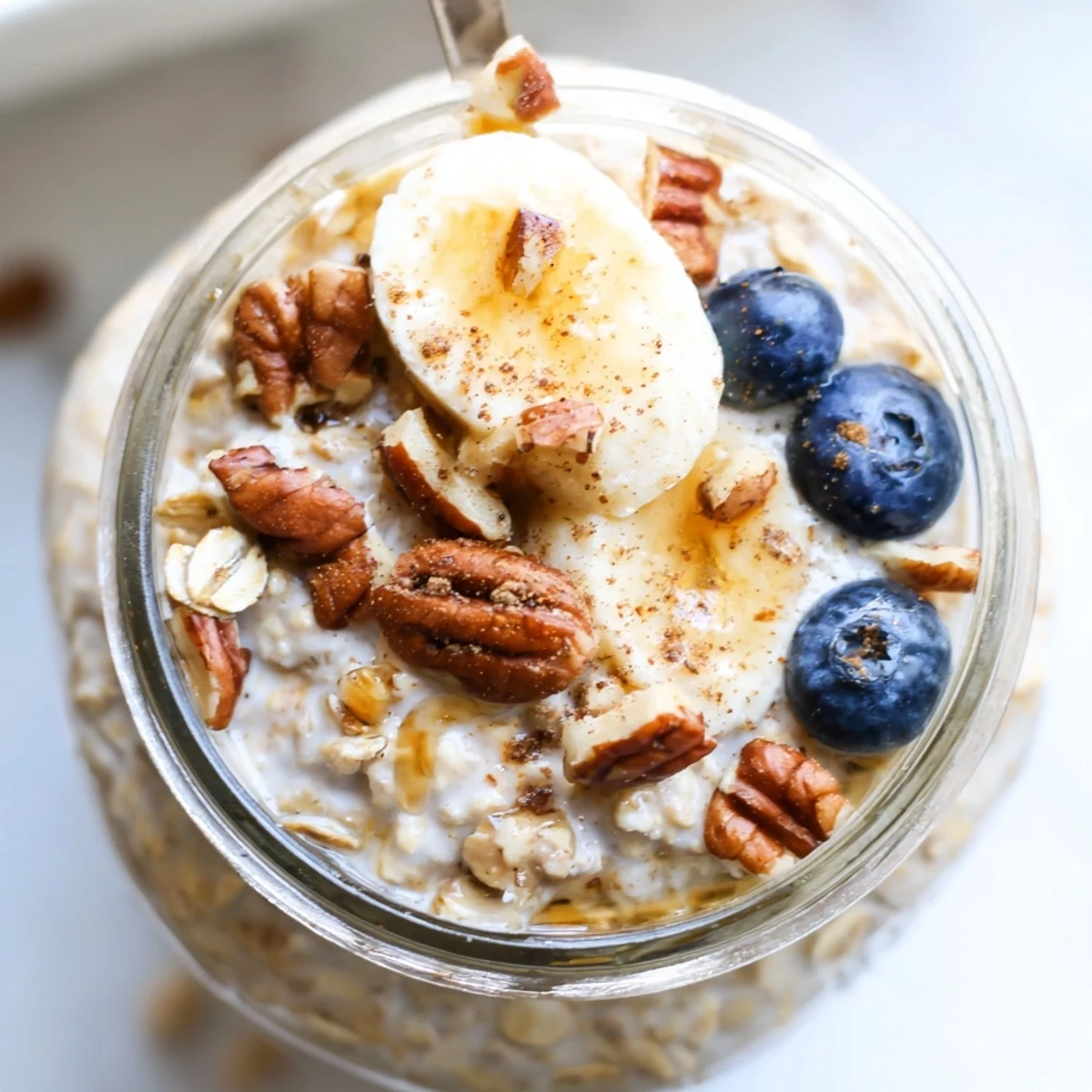 Thick maple cinnamon pecan overnight oats swirled with warm spices, crowned with toasted pecans in a glass jar