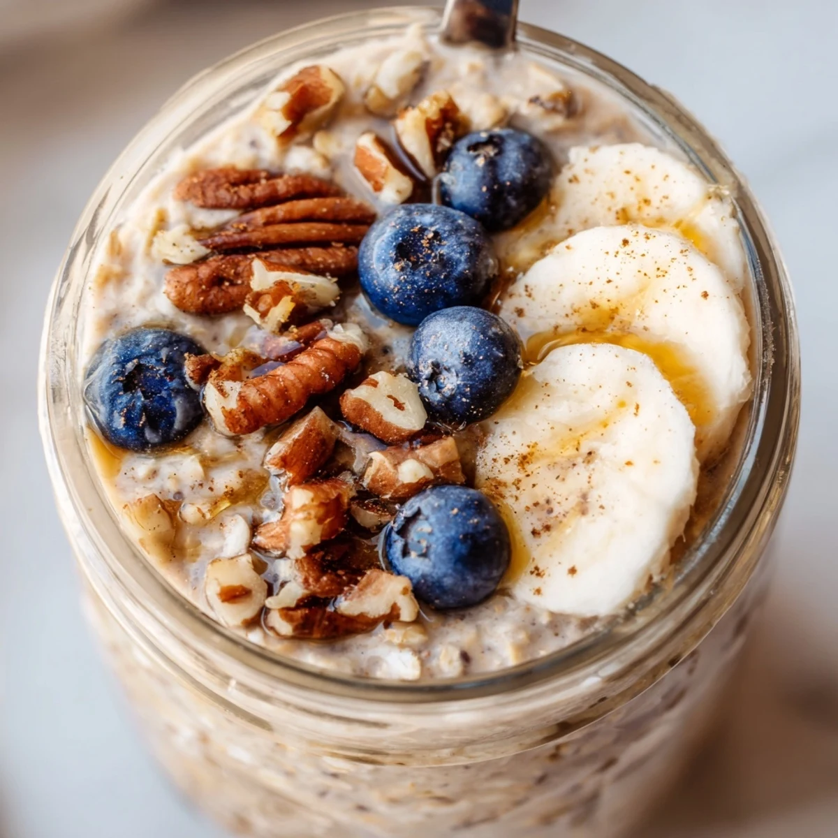 Chilled maple cinnamon pecan overnight oats nestled in a jar, finished with a cinnamon dusting and fresh berries