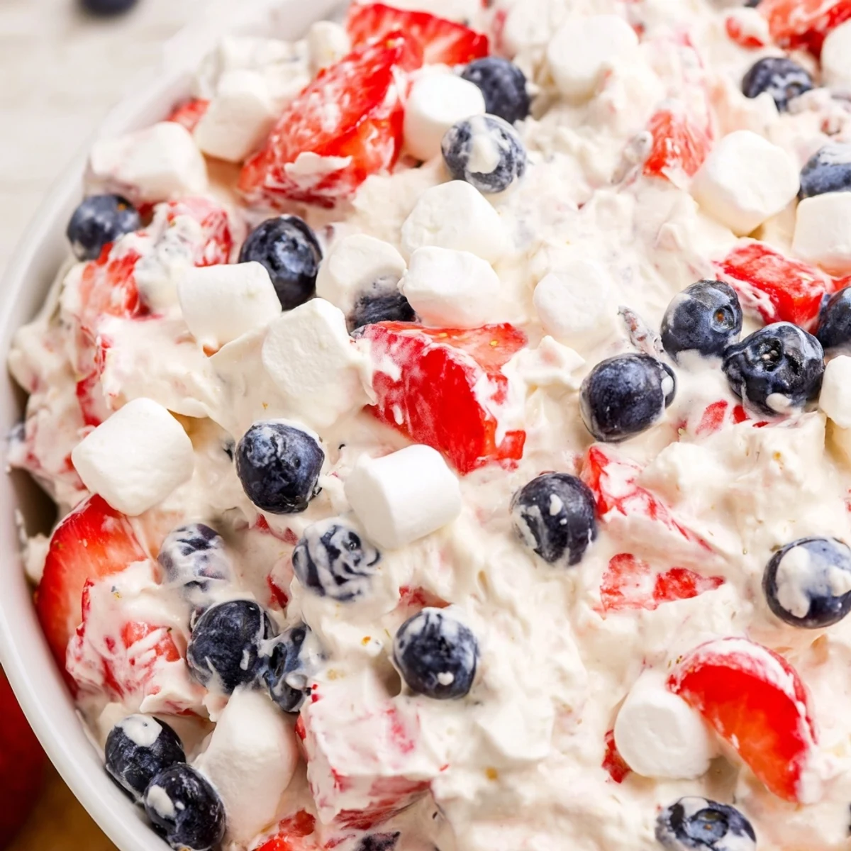 Creamy Red White Blue Cheesecake Salad topped with fresh strawberries and blueberries