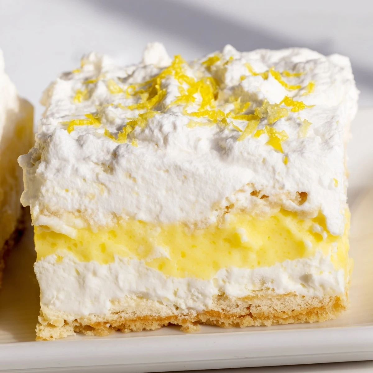 Chilled Lemon Lush Cake served on white plate, garnished with fresh lemon zest and featuring distinct tri-layer texture